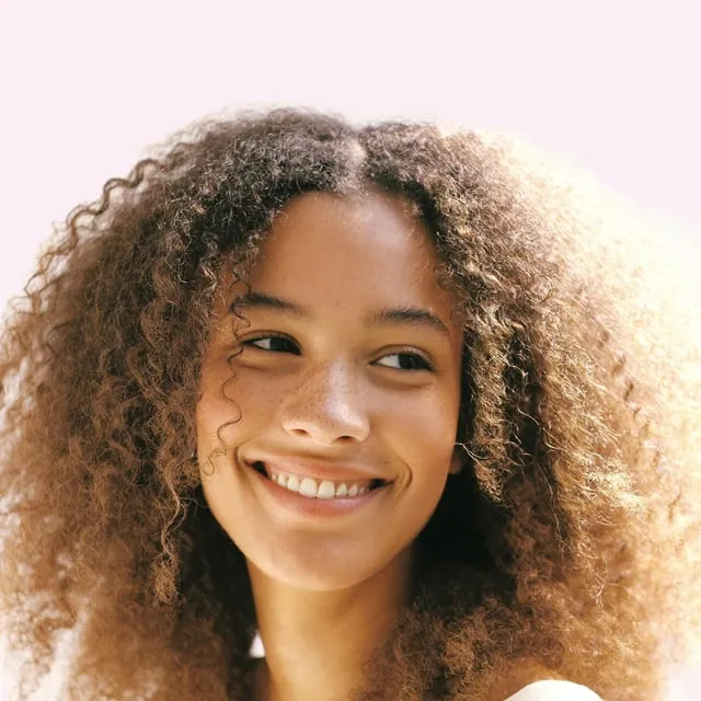 Jeune femme métisse aux grandes boucles châtain miel, grand sourire