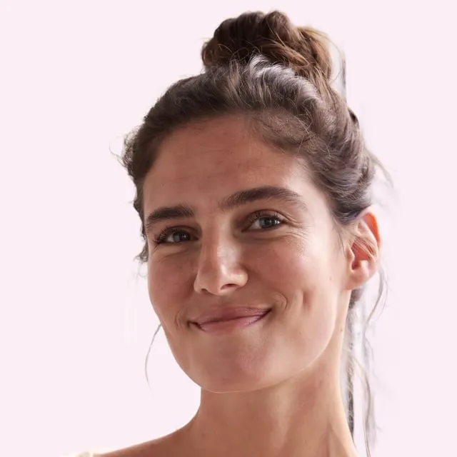 Femme brune aux cheveux relevés en chignon haut, sourire en coin