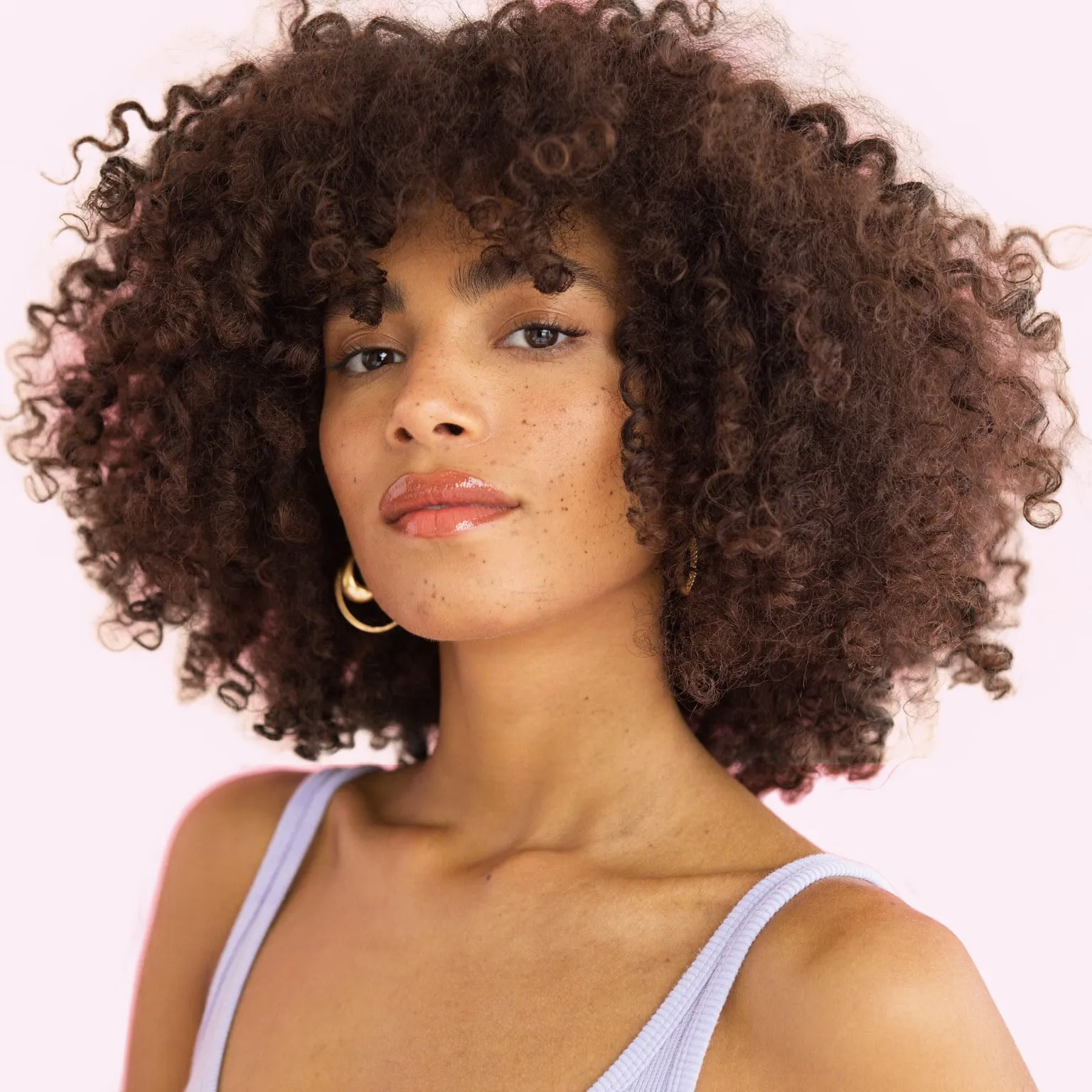 Portrait d’une femme aux cheveux bouclés et taches de rousseur, sur fond rose (visuel généré par IA)